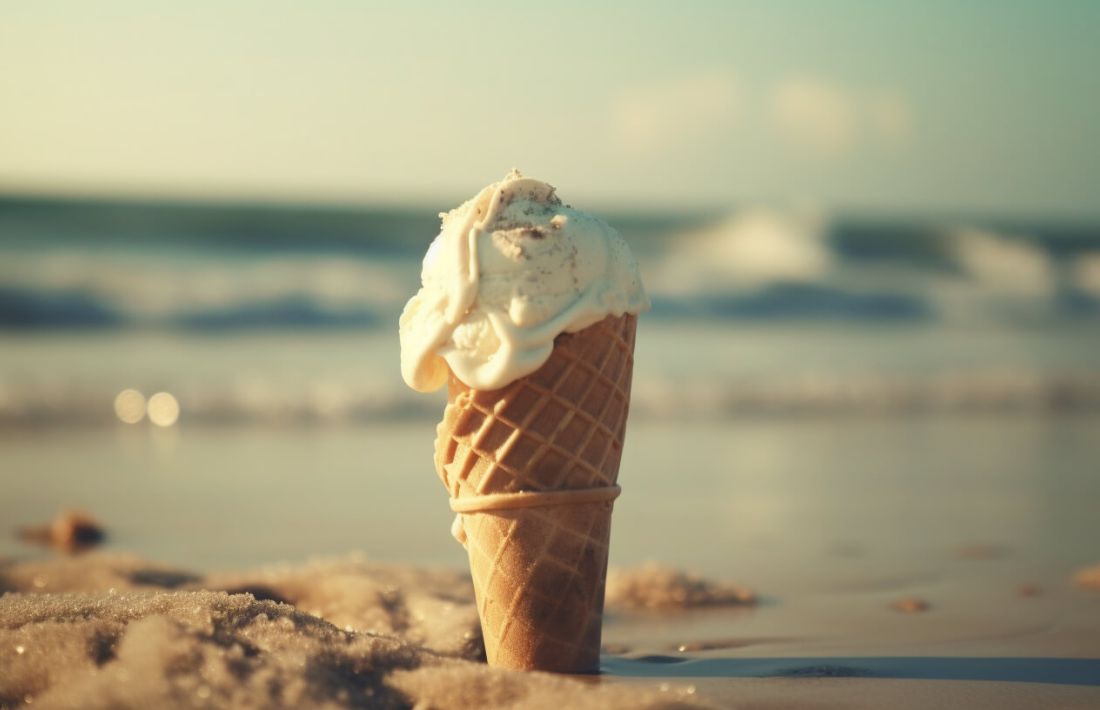 En glass sitter nedstoppad i sanden vid en strand med havet i bakgrunden